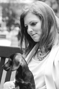 Mental health and well-being in the workplace are the subjects of a session being presented by Laura Capell-Abra, founder of Stress Matters, at IBTM World Barcelona (2021). This black and white photo shows Laura Capell-Abra holding a dog.